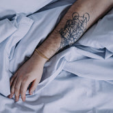 Hand with a tattoo on an arm resting on light blue fabric