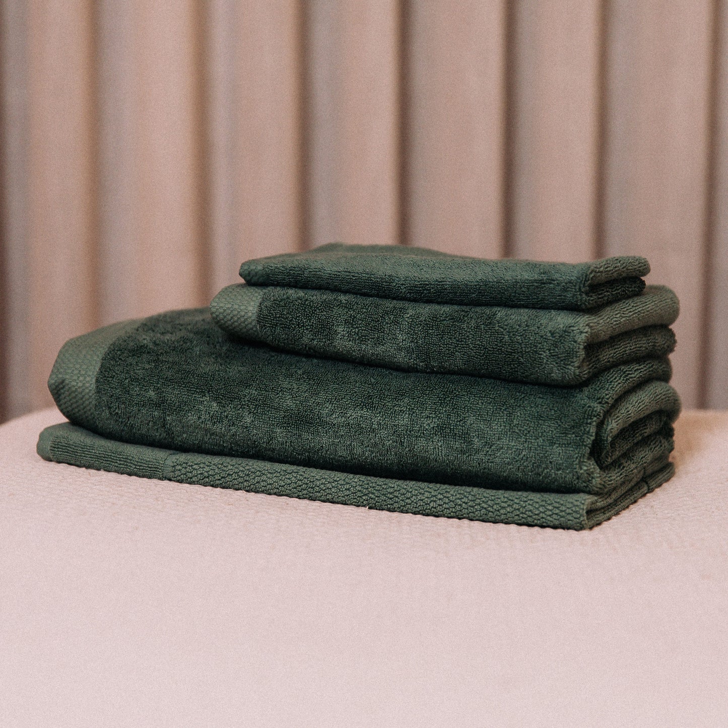 Stack of green towels on a beige surface with a neutral background