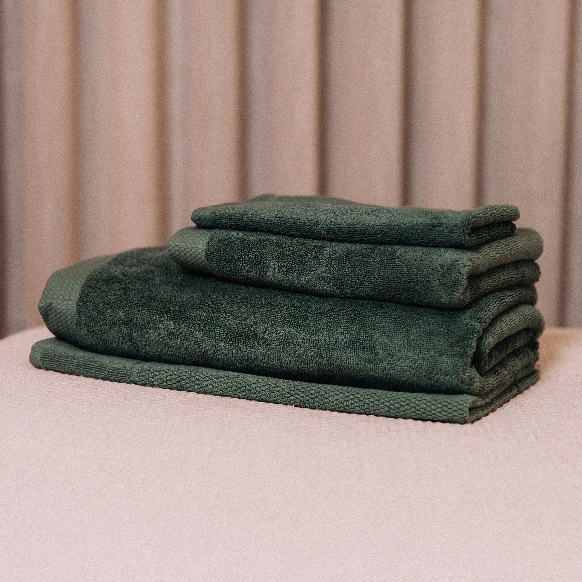 Stack of green towels on a beige surface with a neutral background