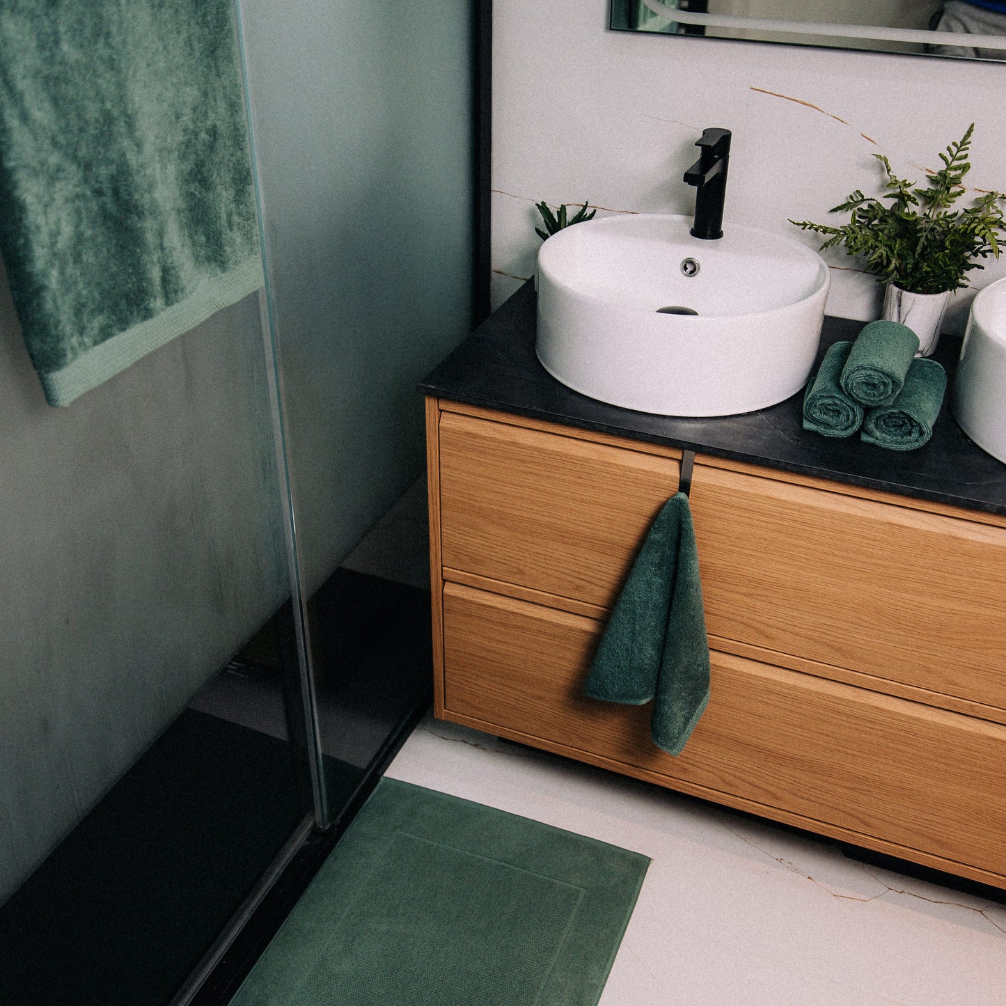 Bathroom with wooden vanity, white sink, and green towels